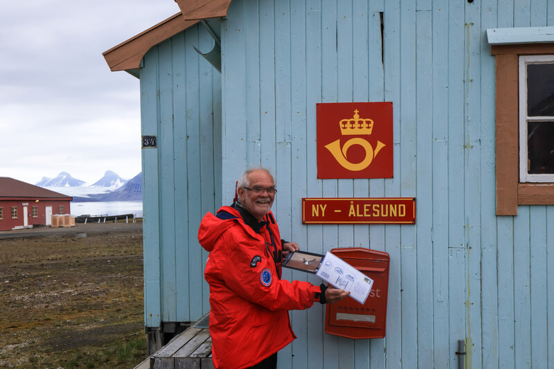 Ein Mann im Expeditions-Parka wirft eine Postkarte in den nördlichsten Briefkasten in Ny-Ålesund